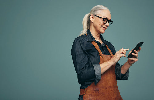 Happy mature goldsmith using a smartphone in a studio
