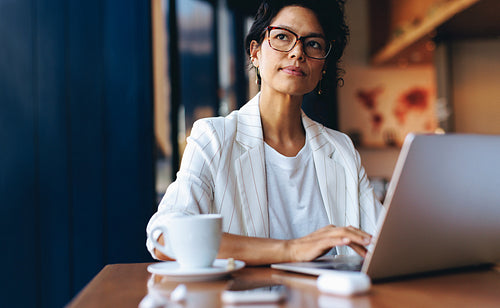 Professional woman working on laptop in a cafe, thinking deeply