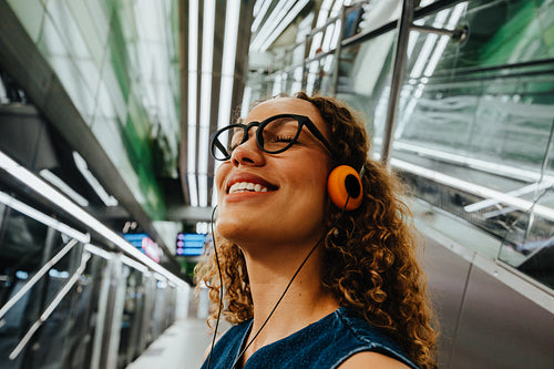 Curly-haired woman enjoys music while commuting in a modern station