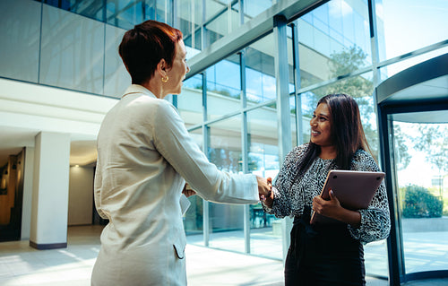 Professional businesswomen shaking hands in a bright modern office lobby