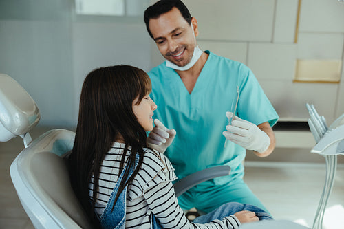 Dentist showing young patient her teeth with a mirror during checkup