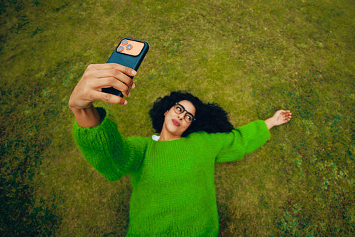 The woman enjoys a quiet outdoor moment as she takes a selfie on grass with her smartphone