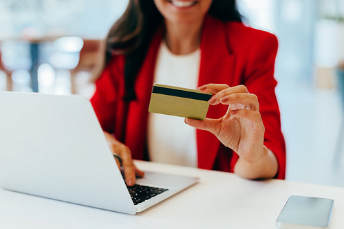 Smiling woman in a red blazer shopping online using a laptop and credit card