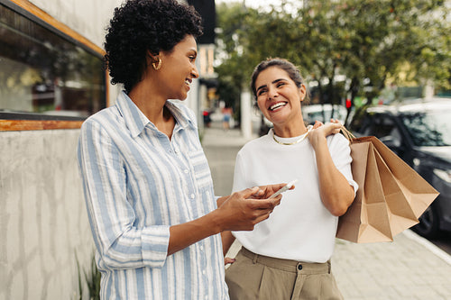 Happy female friends smiling at each other after shopping in the city
