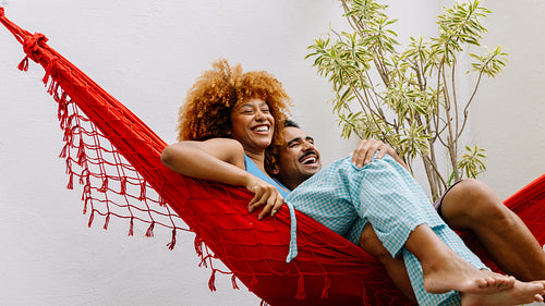 Happy couple relaxing together in a red hammock outdoors under natural light