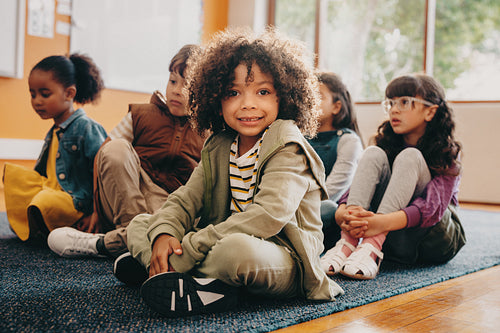 Boy sits in an elementary school class, he is looking at the camera