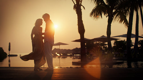 Romantic couple enjoys a beautiful tropical sunset with cocktails by the infinity pool