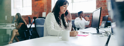 Businesswoman taking notes while on a phone call