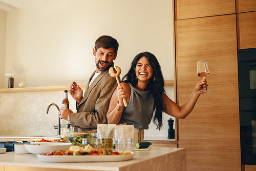 Happy couple enjoying drinks and fun while cooking dinner together