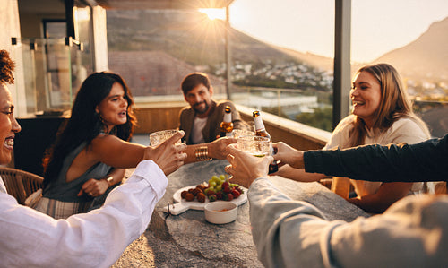 Friends toasting drinks and laughing together on a rooftop during sunset