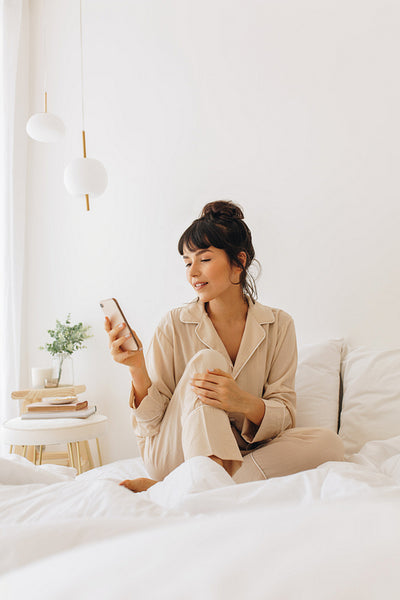 Woman browsing mobile phone sitting on bed