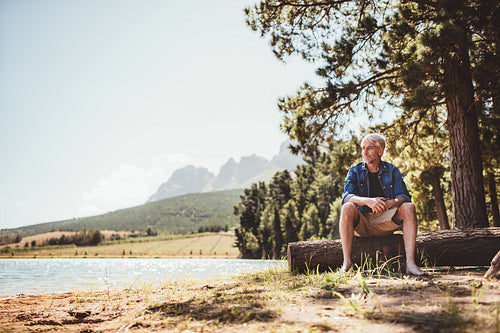 Mature man sitting on wooden log by the lake