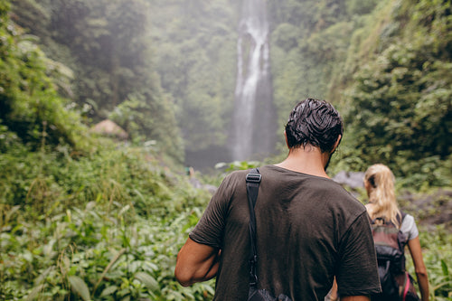 Couple of tourists walking towards a waterfall in forest
