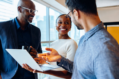 Happy colleagues discussing ideas with a laptop in a bright office