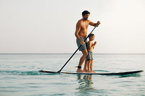 Father and son enjoying paddleboarding together on a serene sea during a sunny holiday