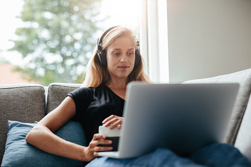 Young woman relaxing on sofa with laptop in living room
