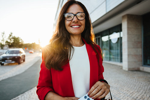 Confident businesswoman in red jacket smiling outdoors in urban setting