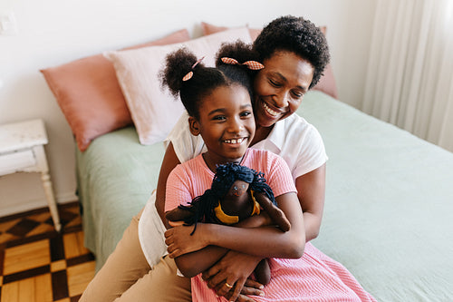Mother hugging her daughter and her doll on the bed