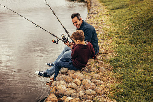 Father and son enjoying fishing sitting near the lake