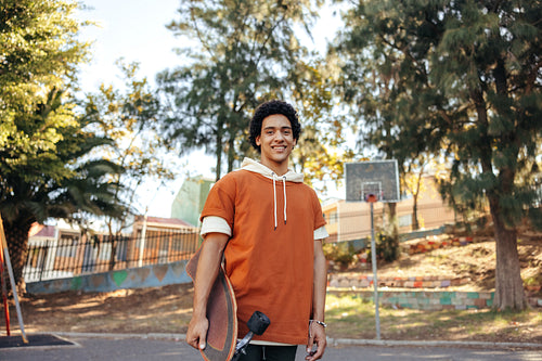 Happy skateboarder carrying his skateboard outdoors during the day