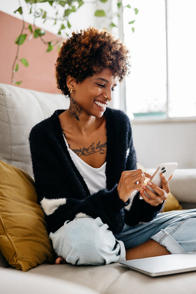 Happy young woman relaxing at home using smartphone