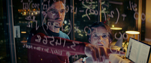 Focused young professionals solve complex equation on glass wall
