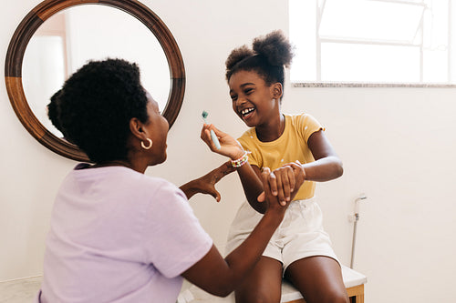 Fun tooth care in the bathroom: Young girl laughing while brushing her teeth with her mother