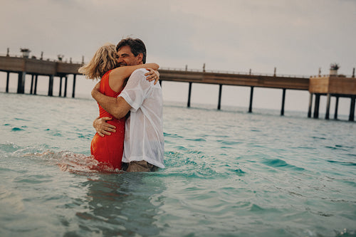 Older couple embracing in the ocean by a pier on a tropical island
