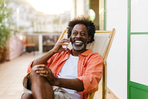 Happy mature man enjoying a phone call on a patio chair