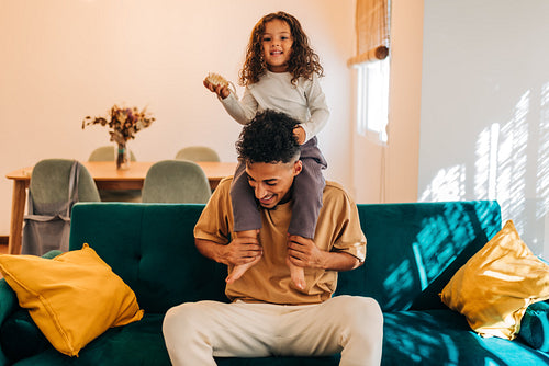 Adorable little girl sitting on her father's shoulders at home