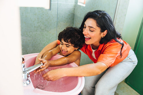 Latina mother helping her happy son wash hands in a pink sink