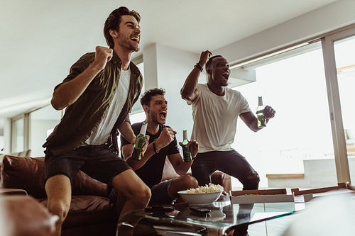 Three friends watching a game on a TV at home