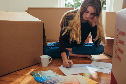 Woman making a list of articles sitting on floor with shade cards and coffee