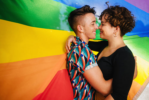 Romantic queer couple bonding against a rainbow flag