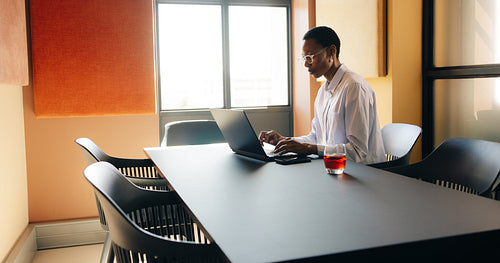 Young professional working at a modern office desk with a laptop and drink