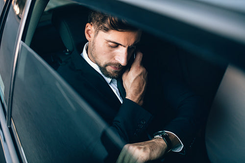 Businessman travelling by car checking time and talking on cellphone