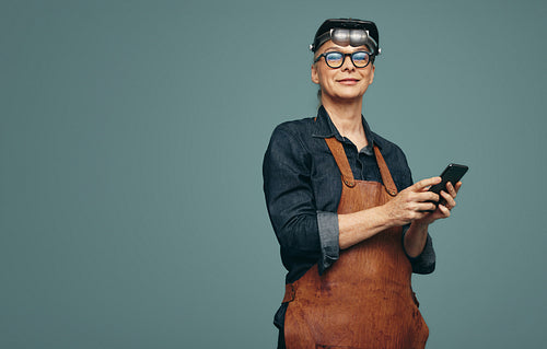 Mature jewellery maker holding a smartphone in a studio