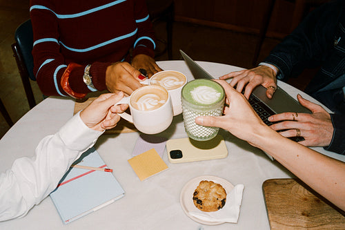 Friends toasting lattes while working on laptop