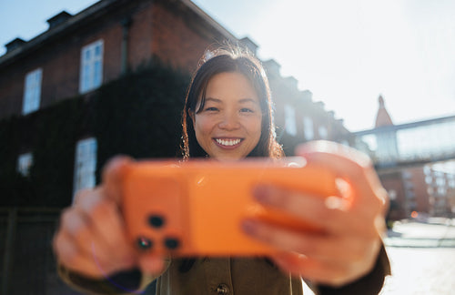 Woman taking a smiling selfie with smartphone outdoors