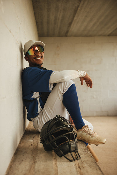 Smiling baseball player in uniform sitting in dugout with bat and helmet