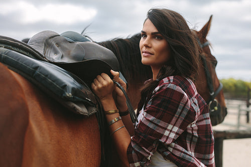 Woman fixing a saddle on her horse