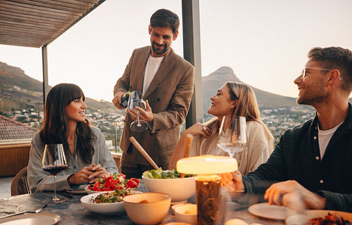 Man pouring wine for friends on an outdoor terrace during sunset