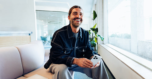 Businessman with phone in office smiles