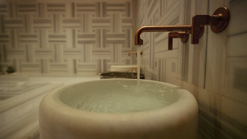 Water flowing from a modern copper faucet into a sleek marble basin in a luxury spa