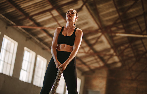 Woman exercising with battling rope at old factory shade
