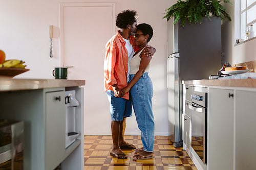 Romantic husband holding his wife close in his arms, showing her love and affection in their home kitchen