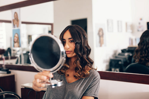 woman in salon with curled hairstyle looking herself in mirror