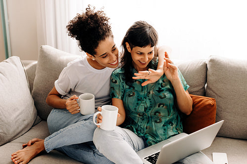 Happy lesbian couple video calling their friends at home