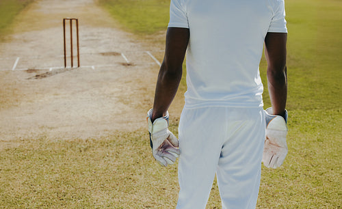 Cricketer in uniform standing on the pitch with gloves near stumps