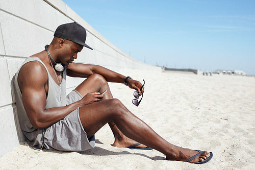 Young african guy sending a text message at the beach